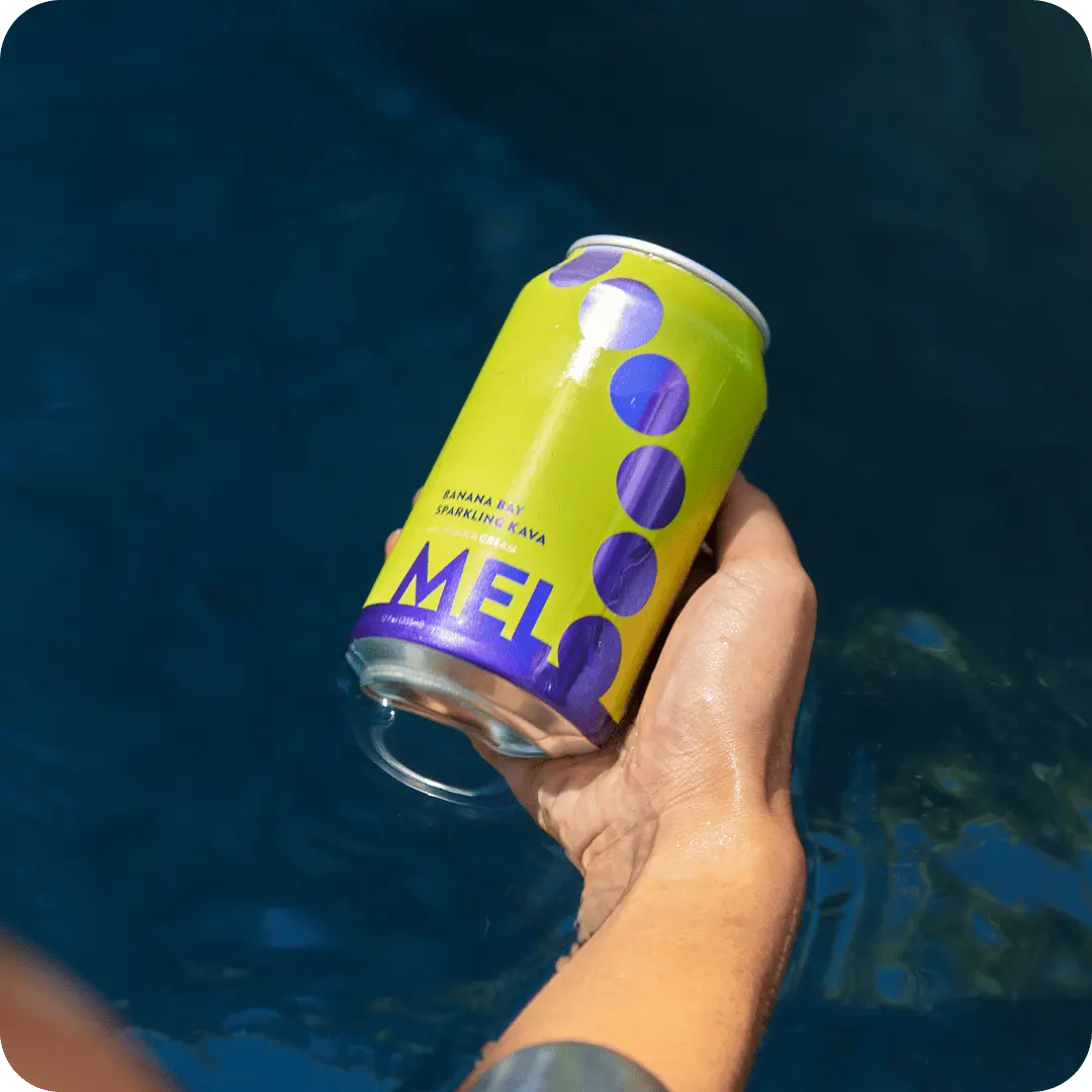 A hand holding Melo Banana Bay sparkling kava can over water, emphasizing the vibrant and refreshing nature of the drink.