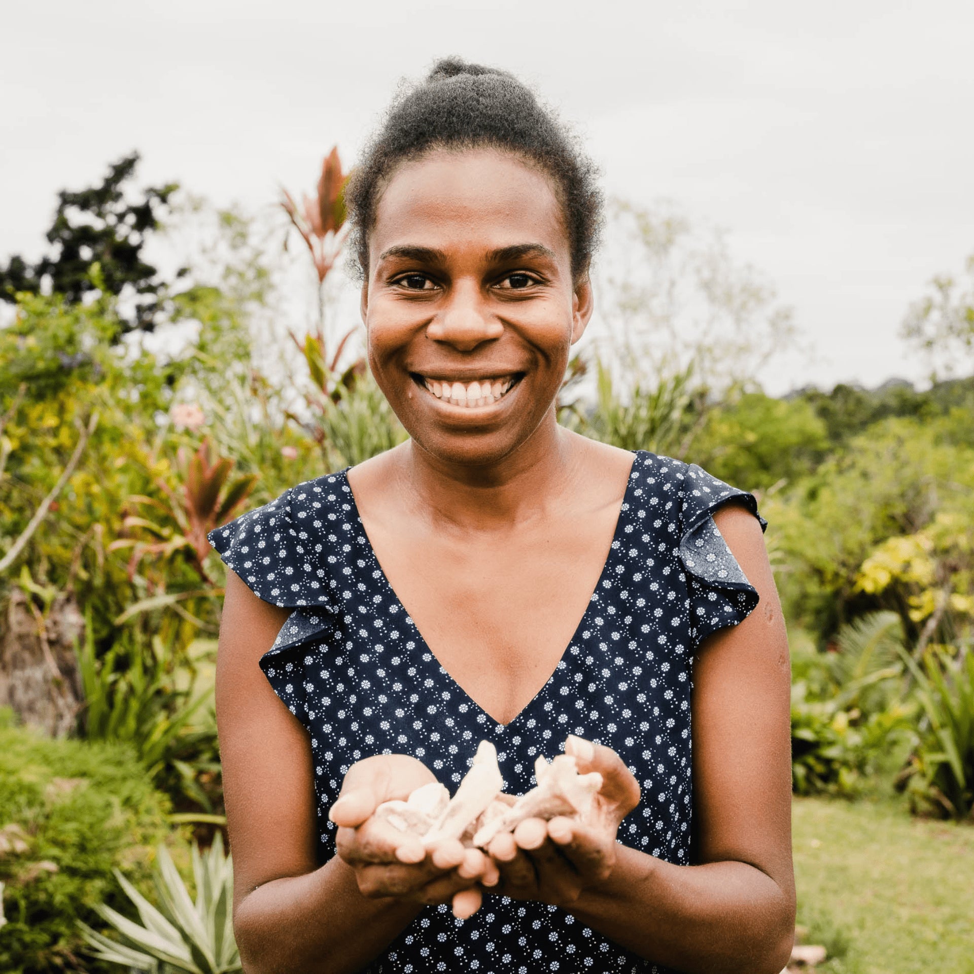 Smiling woman holding kava roots in Vanuatu, representing Melo’s ethical farming practices and connection to the local community.